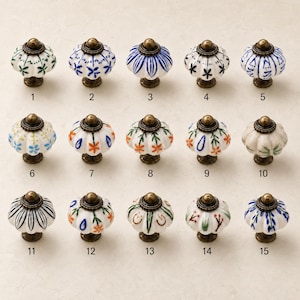 May include: A collection of fifteen round, fluted ceramic cabinet knobs, each featuring unique hand-painted floral or geometric patterns in blue, green, orange, and black. Each knob is topped with a small, dark bronze-toned metal cap and base.