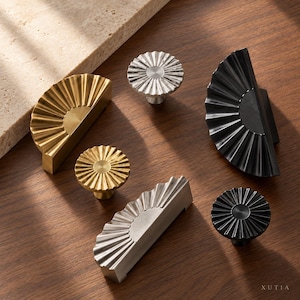 May include: A collection of metal cabinet hardware including three semi-circular fan-shaped pulls and three circular knobs in gold, silver, and black finishes. Each piece features a radial ribbed texture and a central circular detail. The text XUTIA is visible in the bottom right corner.