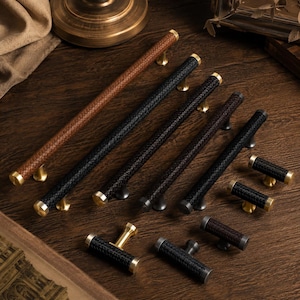 May include: A collection of cabinet hardware including long bar pulls and T-shaped knobs. The handles feature a textured, woven-style pattern in black and brown, accented with metallic gold or dark grey cylindrical end caps and mounting posts.