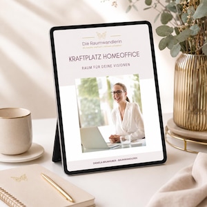 May include: A tablet displaying a document titled Die Raumwandlerin KRAFTPLATZ HOMEOFFICE RAUM FÜR DEINE VISIONEN with a photograph of a person in a white shirt using a laptop. The tablet is positioned on a desk with a notebook and a pen.