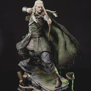 Pode incluir: Uma estatueta detalhada de um arqueiro elfo de cabelos longos com túnica e capa verdes, segurando um arco e flecha de madeira. O personagem está sobre uma base rochosa com detalhes em corda, vestindo calças e botas escuras.
