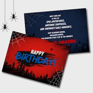 May include: Two rectangular birthday cards featuring a comic book aesthetic. One card is red with a black city skyline, spiderwebs, and the text HAPPY BIRTHDAY in blue. The other is dark blue with a city skyline, spiderwebs, and inspirational text.