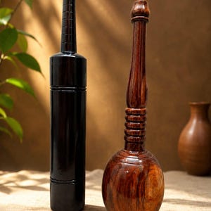 Può includere: Due oggetti in legno posizionati verticalmente. A sinistra, una clava cilindrica liscia color marrone scuro con linee orizzontali scanalate vicino alla sommità. A destra, un utensile in legno lucido color marrone rossiccio con collo lungo.