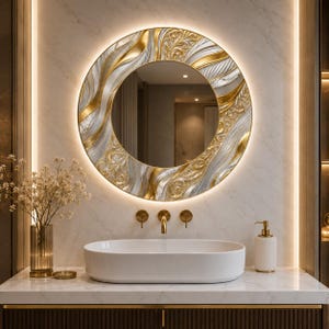 May include: A round wall mirror featuring a decorative frame with swirling gold and silver textured patterns. The mirror is backlit with integrated LED lighting, creating a glowing halo effect against the wall behind the white oval basin.