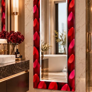 May include: A rectangular wall mirror featuring a wide frame decorated with a repeating pattern of vibrant red and pink lipstick tubes. The central glass panel is clear and reflective, showing a view of a bathroom interior.