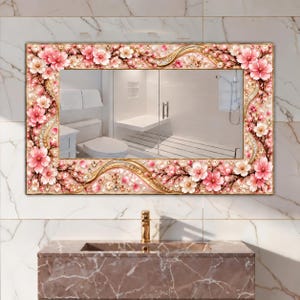 May include: A rectangular wall mirror featuring a decorative frame adorned with pink and white cherry blossom flowers, gold swirling accents, and embedded clear crystals. The mirror reflects a bathroom interior with a toilet and shower stall.