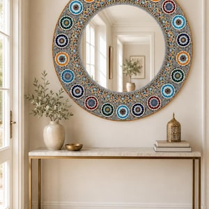 May include: A large circular wall mirror featuring a wide, decorative frame adorned with a repeating pattern of colorful, intricate floral mandalas in shades of blue, red, green, and yellow, set against a dark, detailed mosaic background.