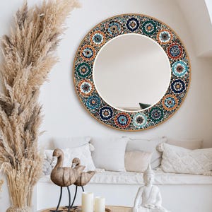 May include: A circular wall mirror featuring a wide frame decorated with a repeating pattern of colorful floral mandalas in shades of deep blue, teal, orange, and white. The mirror has a smooth, reflective glass center and a thin gold-toned edge.