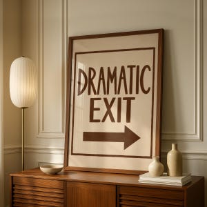 May include: A framed rectangular wall art piece featuring a cream background with the dark brown text DRAMATIC EXIT and a dark brown arrow pointing to the right. The artwork is enclosed in a simple dark wood frame with a clean border.