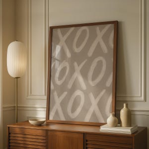 Peut inclure: Une impression d'art murale rectangulaire dans un cadre en bois foncé présentant un motif répétitif de lettres X et O peintes au pinceau blanc sur un fond taupe sourd. L'œuvre est présentée verticalement avec une texture visible des traits.