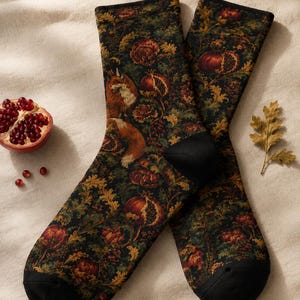 May include: A pair of crew socks featuring a dark green background with a repeating pattern of orange foxes, red pomegranates, and golden oak leaves. The socks have solid black cuffs, heels, and toes, showcasing a detailed botanical illustration.