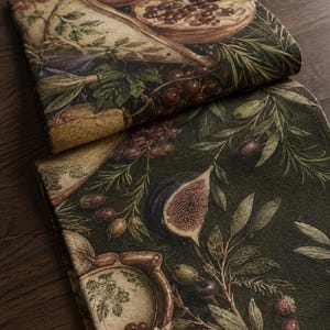 May include: A folded fabric runner featuring a detailed botanical print of pomegranates, figs, and olives. The design showcases deep green foliage, dark purple fruit, and earthy brown accents on a textured textile surface with visible stitching.