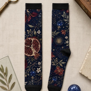 May include: A pair of crew socks featuring a dark navy blue background with a detailed botanical and celestial print. The pattern includes red pomegranate halves, dark red flowers, white blossoms, golden sunbursts, and blue spheres.