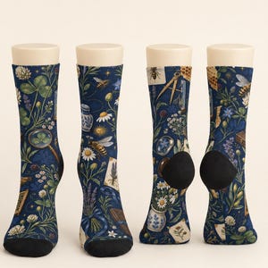 May include: Four crew socks with a dark blue background featuring a botanical and scientific pattern. The print includes bees, honeycombs, magnifying glasses, compasses, white flowers, lavender sprigs, and small blue and white ceramic vases.