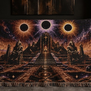 Puede incluir: Una manta tejida que presenta una escena detallada de un gran templo con dos grandes estatuas sentadas flanqueando una escalera central. Sobre la estructura, tres eclipses circulares oscuros brillan contra un cielo cósmico púrpura y naranja.