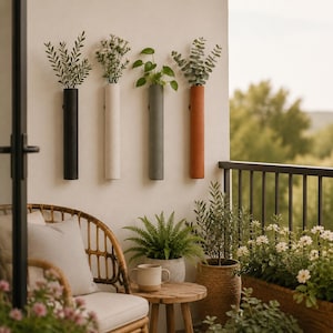 May include: Four cylindrical wall-mounted planters in black, white, gray, and terracotta, each holding green foliage or small flowers. These vertical tube-shaped vessels are attached to a light-colored wall, creating a linear display of plants.