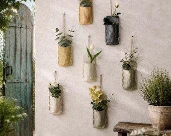 May include: Six wall-mounted hanging pouches in various neutral colors, each featuring visible side stitching and a thin cord for suspension. These pouches hold assorted green plants and flowers, including white tulips and yellow blossoms.