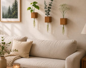 May include: Three wall-mounted wooden block planters with clear glass test tube inserts. Each wooden cube holds a different plant: a green leafy plant, a sprig of eucalyptus, and white baby's breath flowers, all with visible stems in water.
