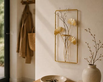 May include: A rectangular gold metal wall-mounted frame featuring a clear glass test tube vase. The frame is decorated with three metallic gold ginkgo leaf accents and contains thin, dark brown bare branches arranged within the glass tube.