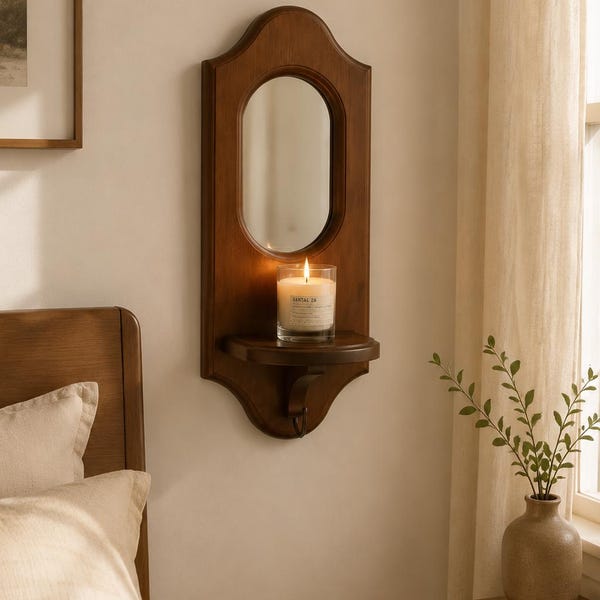 May include: A wall-mounted wooden mirror featuring an arched top and a small integrated shelf. A glass candle holder with a lit white candle sits on the shelf. The mirror frame has a smooth, dark brown finish and a curved, decorative silhouette.