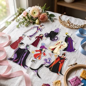 May include: A collection of embroidered patches featuring various animated villain characters in colorful outfits, including figures in purple, red, black, and white attire, arranged on a white fabric surface with a gold tiara and floral accents.