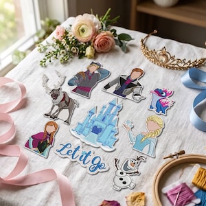 May include: A collection of embroidered patches featuring characters and a castle from the movie Frozen, including a reindeer, a snowman, and the text Let it Go in blue script, arranged on a white fabric surface with ribbons and a tiara.