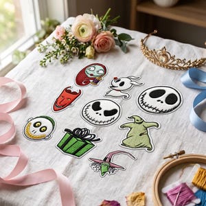 Op de afbeelding: Een verzameling geborduurde patches met personages en iconen uit The Nightmare Before Christmas, waaronder Sally, Zero, Jack Skellington, Oogie Boogie, een groene geschenkdoos, een rood duivelsmasker en een heksenhoed op witte stof.