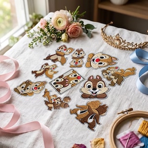 May include: A collection of embroidered fabric patches featuring Chip and Dale in various poses, including full-body figures, head portraits, and a rectangular frame design, arranged on a white fabric surface with flowers and a gold tiara.