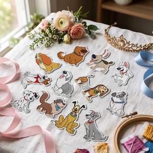 Op de afbeelding: Een verzameling van twaalf geborduurde patches met diverse getekende hondfiguren, waaronder een gevlekte dalmatiër, een golden retriever, een grijze terriër en een speelgoedhond met een veer, gerangschikt op een witte stoffen ondergrond met bloemen en een tiara.