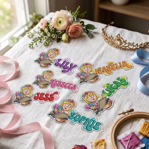 Könnte beinhalten: Sechs gestickte Aufnäher mit einer Zeichentrickfigur mit blonden Haaren, die Blumen und ein Buch hält, jeweils mit einem individuellen Namen: Lily in Lila, Isabella in Orange, Rebecca in Pink, Jess in Rot, Lucas in Grün und Sophie in Türkis.