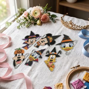 May include: Six embroidered patches featuring Disney characters dressed in Halloween costumes, including Mickey and Minnie Mouse, Donald and Daisy Duck, Goofy, and Pluto, all wearing witch hats or pumpkin accessories on a white fabric surface.