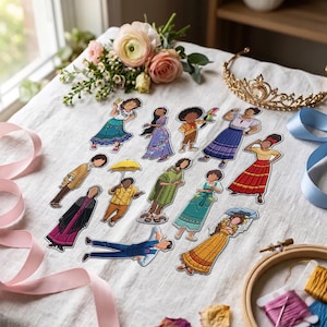 May include: A collection of twelve embroidered character patches featuring diverse figures in colorful outfits, including dresses, ponchos, and shirts. The patches are arranged on a white fabric surface alongside a gold tiara and embroidery hoop.