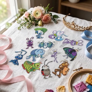 Op de afbeelding: Een verzameling geborduurde patches met diverse insectenpersonages uit de film A Bug's Life, waaronder mieren, een rups, een kever en een vlinder, gerangschikt op een witte stoffen ondergrond met bloemen en een gouden tiara.