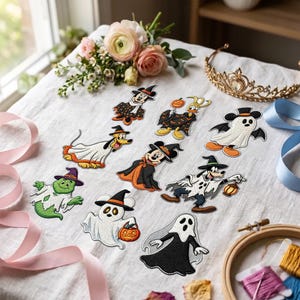 May include: A collection of ten embroidered patches featuring various cartoon characters dressed in Halloween costumes, including ghosts, witches, and vampires, arranged on a white fabric surface alongside a gold tiara and floral accents.