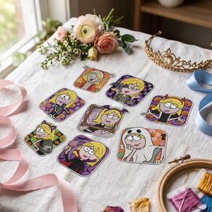 Op de afbeelding: Een verzameling van acht vierkante stickers met een blonde stripfiguur in verschillende Halloween-kostuums, waaronder een mummie, vampier, duivel en geest, gerangschikt op een witte stoffen ondergrond met bloemen en een gouden tiara.