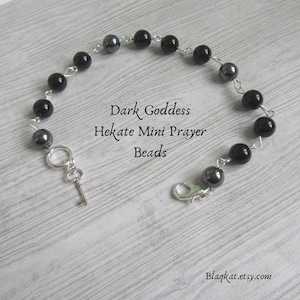 May include: Black and silver prayer beads with a key charm. The beads are labeled "Dark Goddess Hekate Mini Prayer Beads".