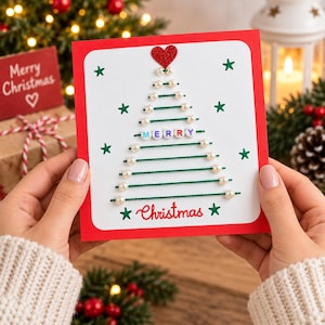May include: A square greeting card with a red border and white center featuring a Christmas tree design made of green thread and white beads. The tree is topped with a red glitter heart and includes the word MERRY in beads and Christmas in red text.
