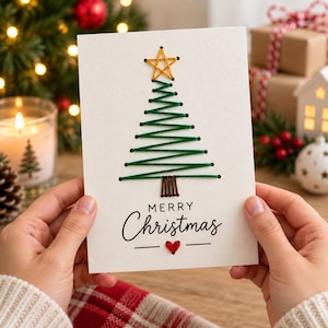 Può includere: Un biglietto d'auguri bianco con un disegno di un albero di Natale ricamato a mano con filo verde, una stella gialla in cima e un tronco marrone. Sotto l'albero, il testo Merry Christmas è stampato in nero, con un piccolo cuore rosso ricamato.