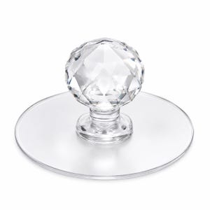 Puede incluir: Un pomo esférico transparente de estilo cristal facetado unido a una base plana circular y transparente. El pomo presenta una superficie geométrica de múltiples facetas que refleja la luz, mientras que la base es lisa y redonda.