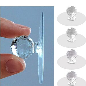 May include: A set of four clear, faceted, spherical knobs, each attached to a flat, circular, transparent adhesive base. The knobs feature a multi-faceted surface that reflects light, and the design includes a clear, round backing for mounting.