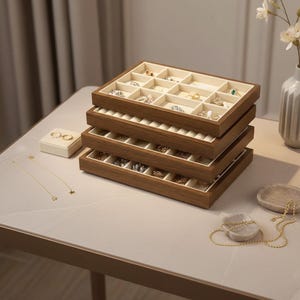 Può includere: Una pila di quattro vassoi portagioie rettangolari in legno con finitura marrone scuro e rivestimento in velluto color crema. I vassoi presentano scomparti di varie dimensioni per organizzare anelli, orecchini e collane con gioielli visibili.