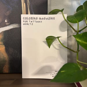 Könnte beinhalten: Ein weißes Malbuch für tätowierte Erwachsene mit schwarzem Text auf dem Einband. Der Einband zeigt den Titel Coloring Magazine For Tattooed Adults und den Text Vol. 1 Illustrated Created By Bli.