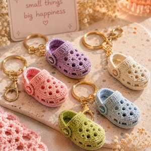 Peut inclure: Cinq porte-clés sabots miniatures au crochet en lavande, crème, rose, bleu clair et vert lime. Chacun possède un anneau en métal doré et un petit bouton circulaire sur le côté avec le texte crocs. Une pancarte indique small things big happiness.
