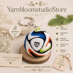 May include: A spherical crochet football keychain featuring a white base with black, blue, orange, and lime green geometric panels. The center panel displays the black text FIFA QUALITY PRO. It includes a silver metal split ring and chain.