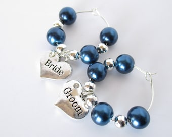 Könnte beinhalten: Zwei silberne Weinglas-Anhänger mit blauen Perlen und herzförmigen Anhängern mit der Aufschrift "Bride" und "Groom".