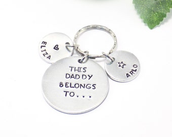 May include: Silver keychain with three round tags. The largest tag says "This Daddy Belongs To..." The other two tags say "Eliza" with a heart and "Arlo" with a star.