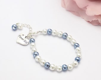 Könnte beinhalten: Ein zartes Armband mit abwechselnd weißen und blauen Kunstperlen, durchsetzt mit kleinen, funkelnden Akzenten. Ein silberner Herzanhänger mit der Aufschrift "Flower Girl" hängt am Armband. Das Armband ist für einen besonderen Anlass gedacht.
