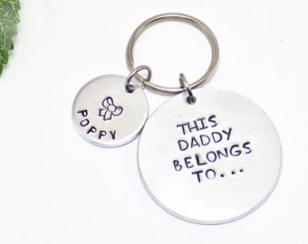 May include: A silver keychain with two circular charms. One charm reads "POPPY" with a bow graphic, the other says "THIS DADDY BELONGS TO..." in black lettering. The keychain is on a white background.