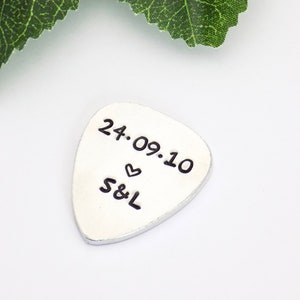 May include: Silver guitar pick with the date "24.09.10" and the initials "S&L" with a heart symbol.