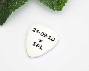 May include: Silver guitar pick with the date "24.09.10" and the initials "S&L" with a heart symbol.